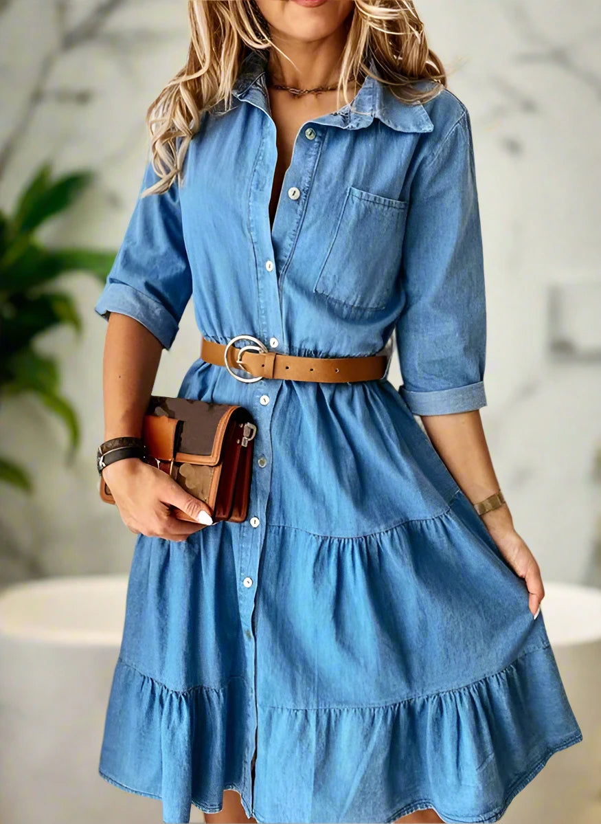 Woman wearing a blue denim dress with a brown belt and holding a brown leather wallet.