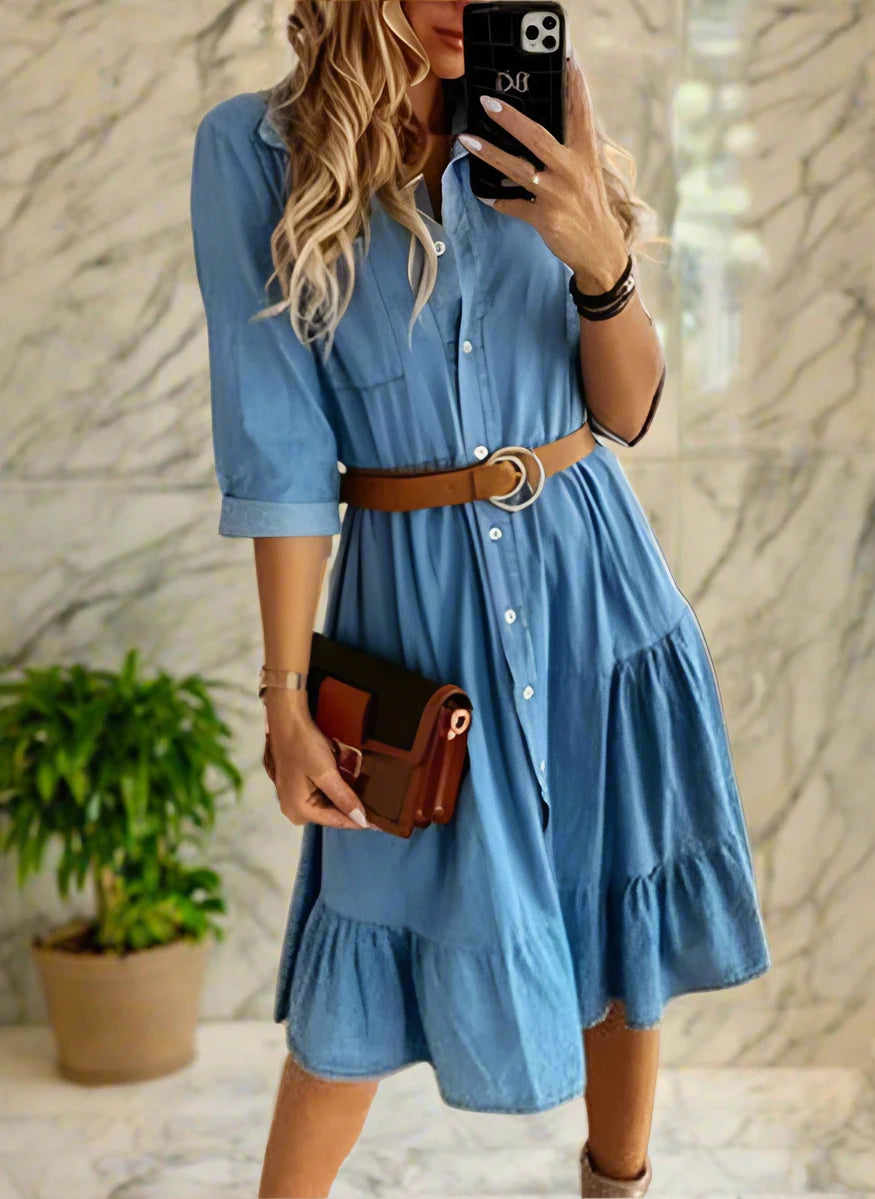 Woman wearing a blue denim dress with a brown belt in a room.
